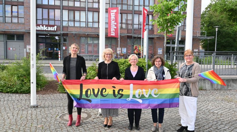 5 Personen halten Regenbogenflagge mit Aufschrift Love is Love