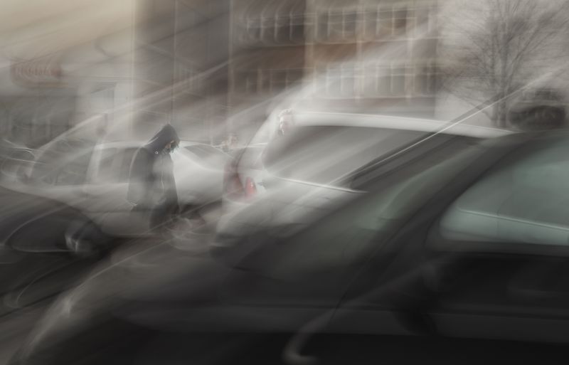Person mit Kapuze auf straße zwischen Autos, verschwommen, Grautöne